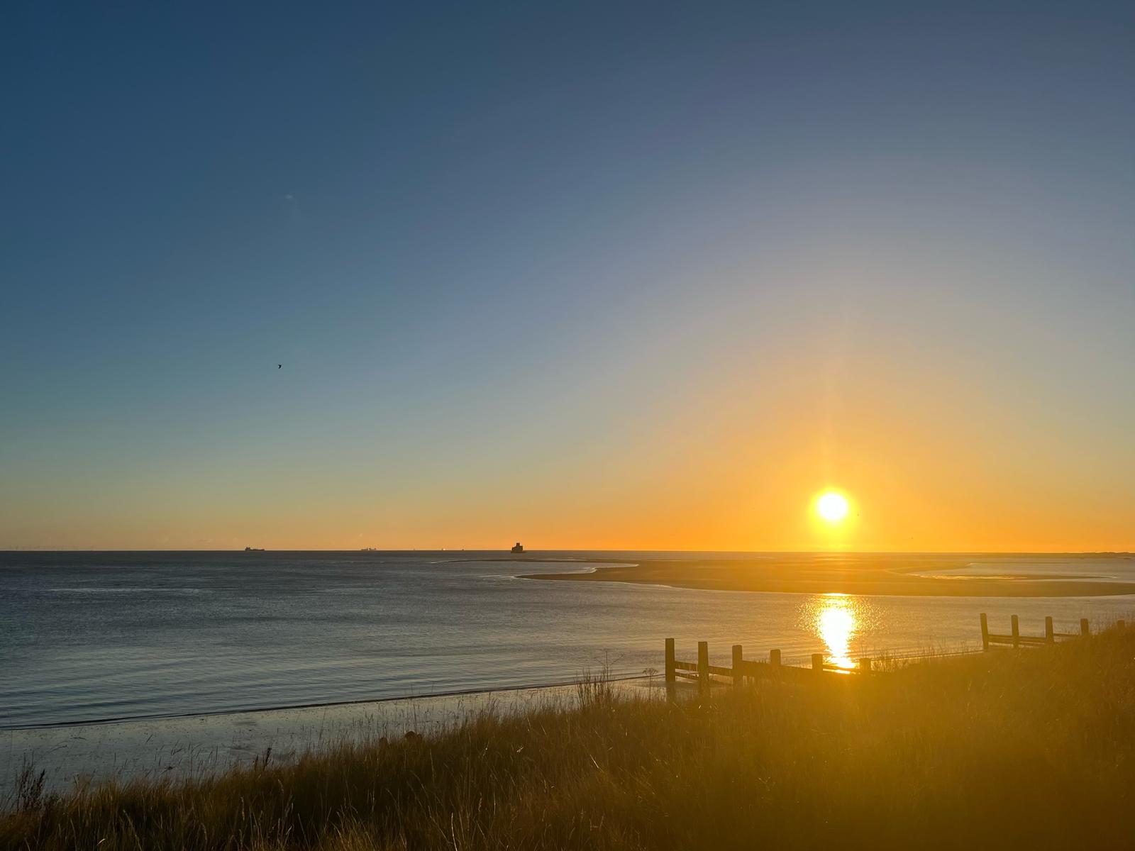 A quiet coastal sunrise over still water.